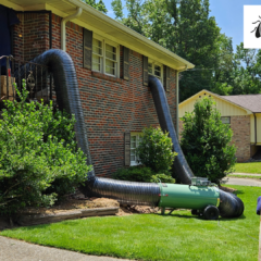 Professional bed bug heat treatment equipment in operation outside a residential brick home, featuring a propane-fired heater, large mylar ductwork running through a window and door, and several propane tanks on the lawn.